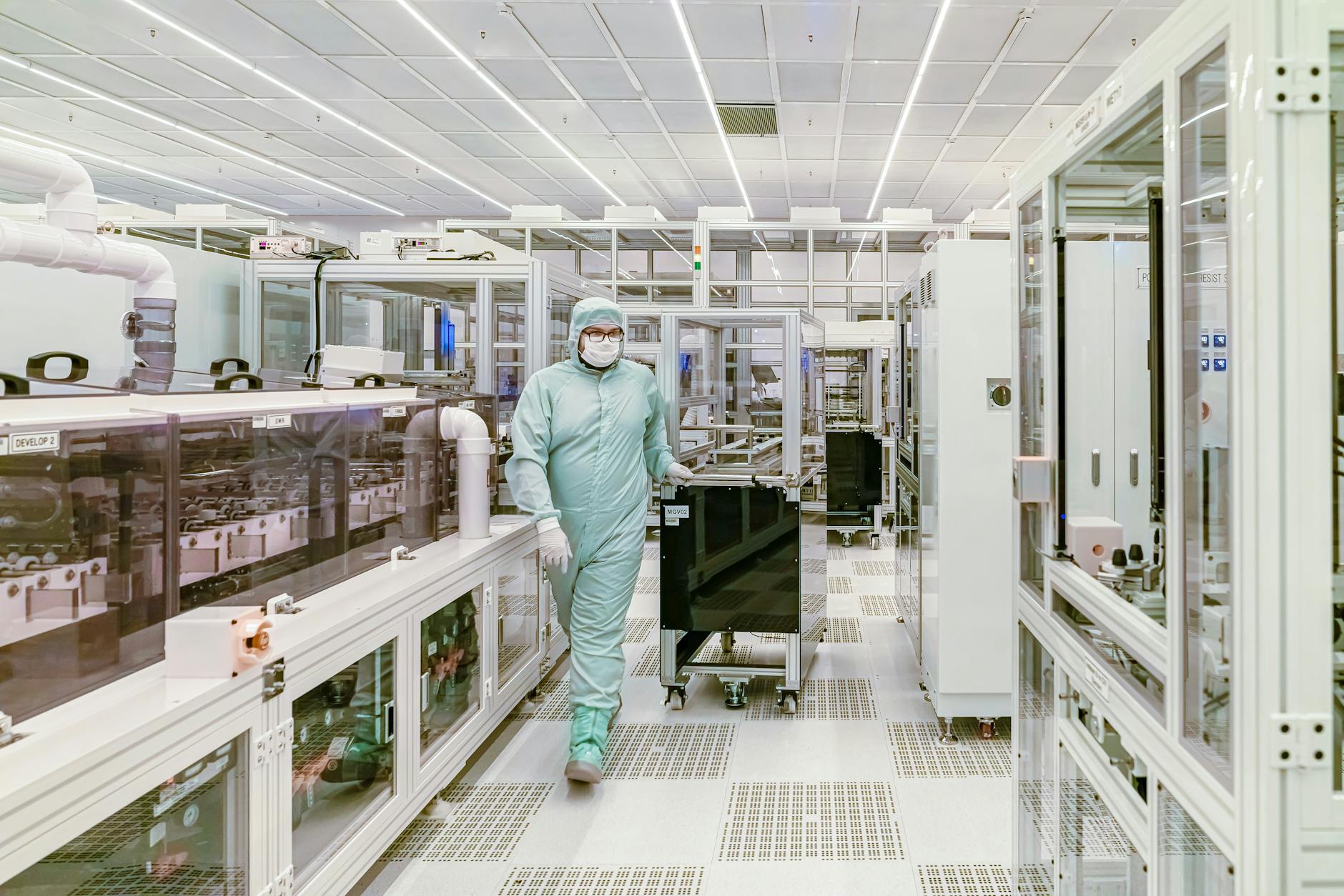Scientist in protective gear walking in a high-tech cleanroom laboratory environment. (Photo by Российский центр гибкой электроники on Pexels)