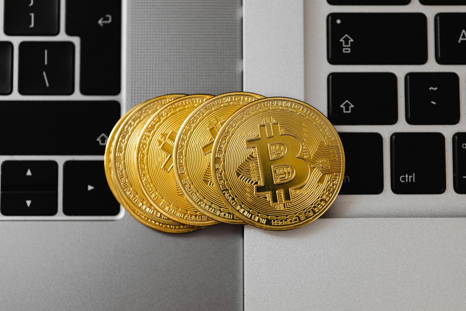 Close-up of Bitcoin coins resting on two laptop keyboards, representing digital currency and tech... (Photo by www.kaboompics.com on Pexels)